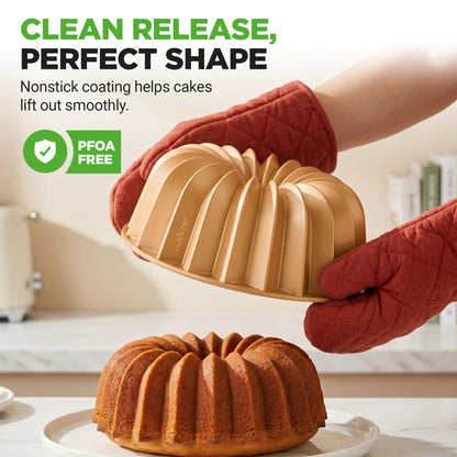 Bundt cake pan with a baked cake, held by a person wearing red oven mitts, on a kitchen counter.